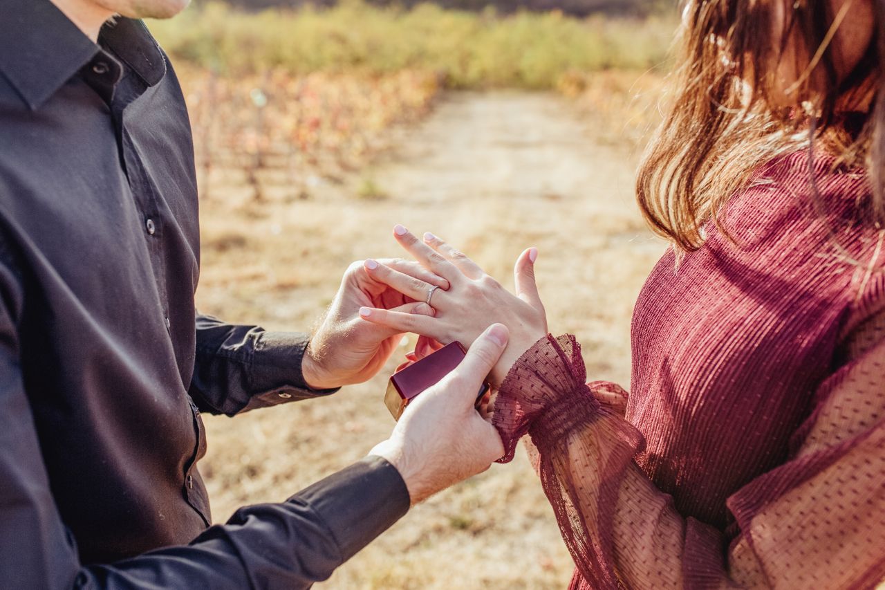 Well-dressed guy slipping an engagement ring on a woman’s finger