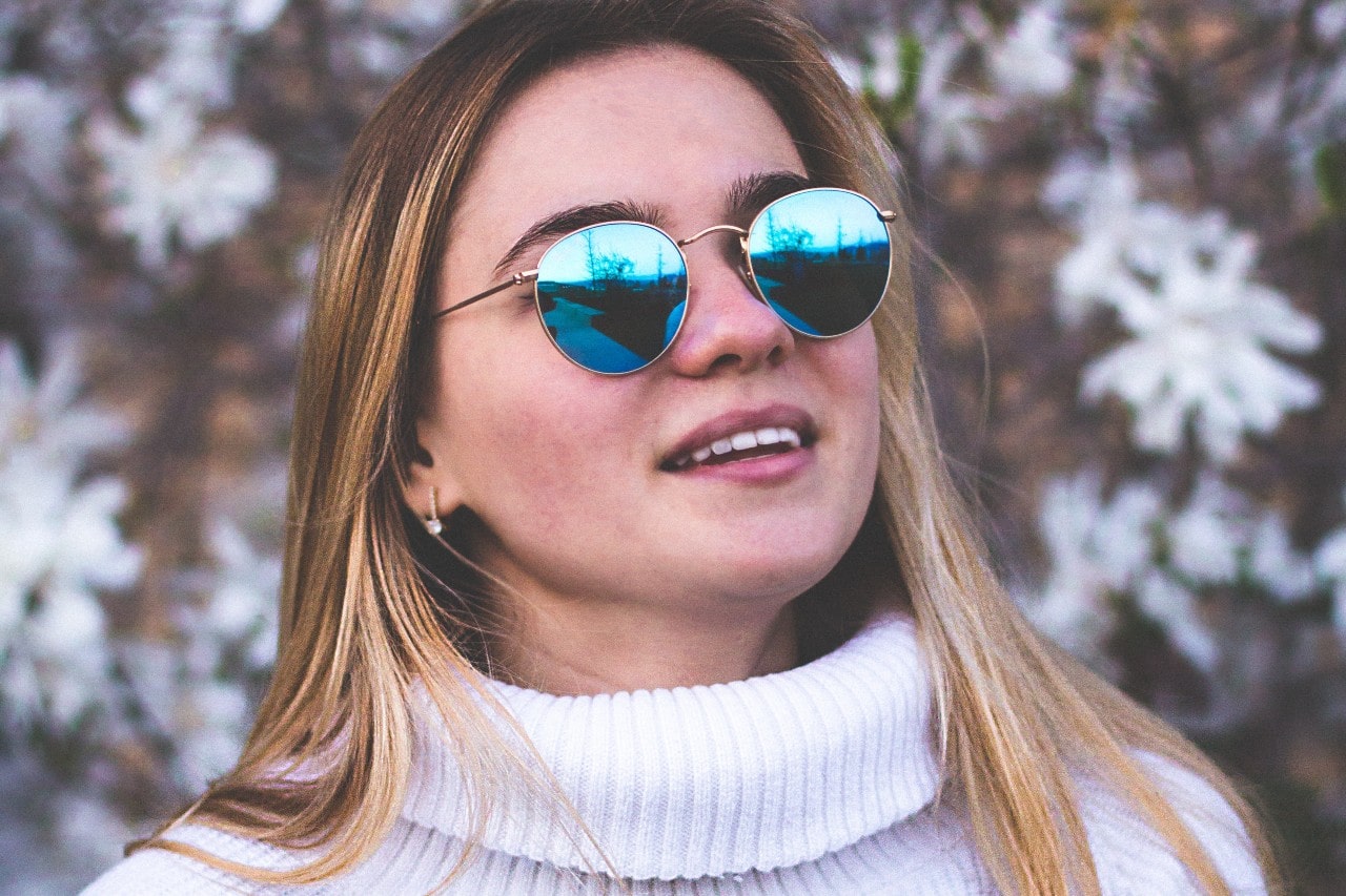 Woman with long, straight blonde hair wearing blue reflective sunglasses, a white turtleneck, and diamond huggies earrings outside Woman with long, straight blonde hair wearing blue reflective sunglasses, a white turtleneck, and diamond huggies earrings outside